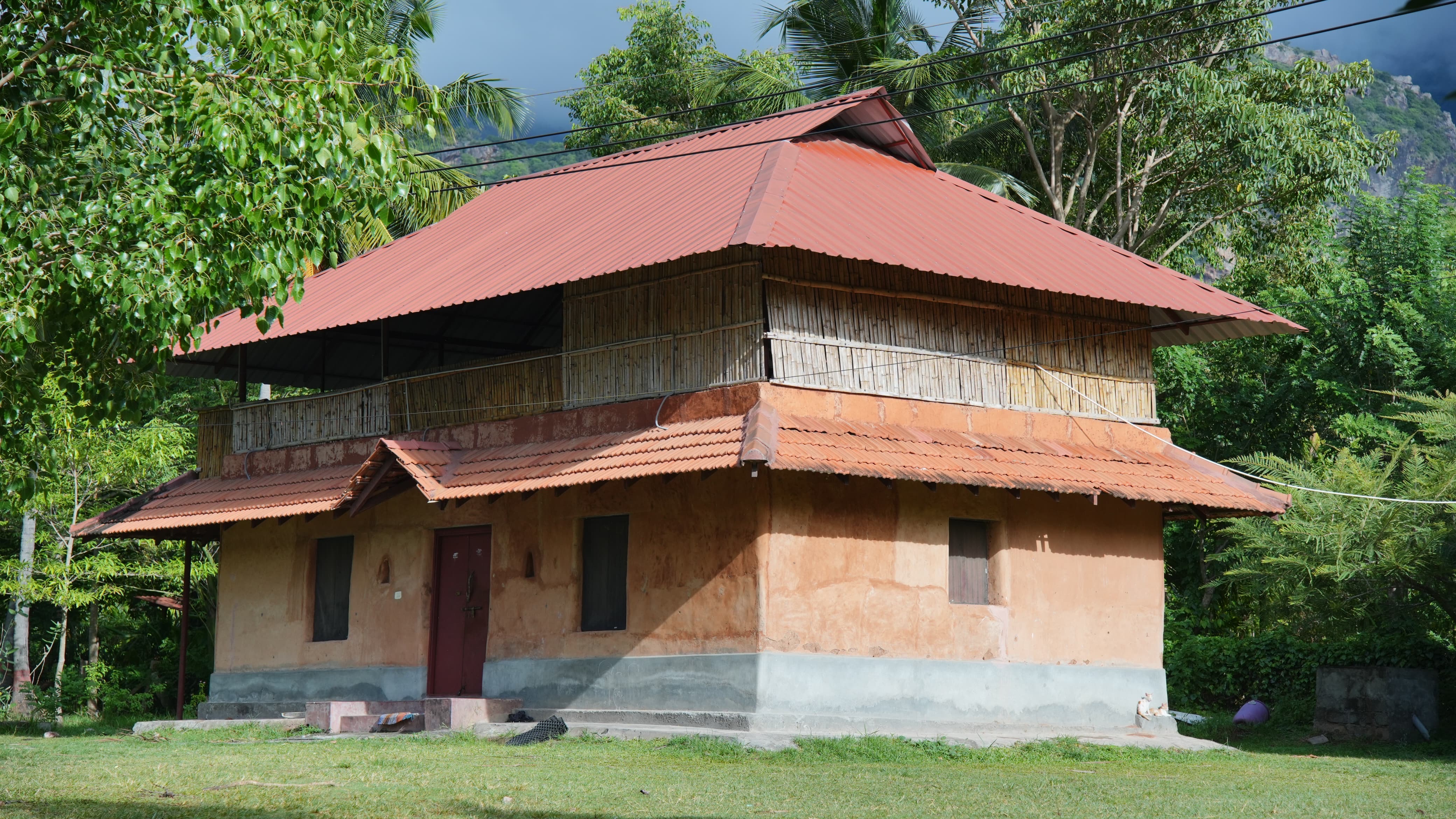 The mud-and-bamboo farmhouse at Iyal Farm, framed by trees at the foothills of the Western Ghats